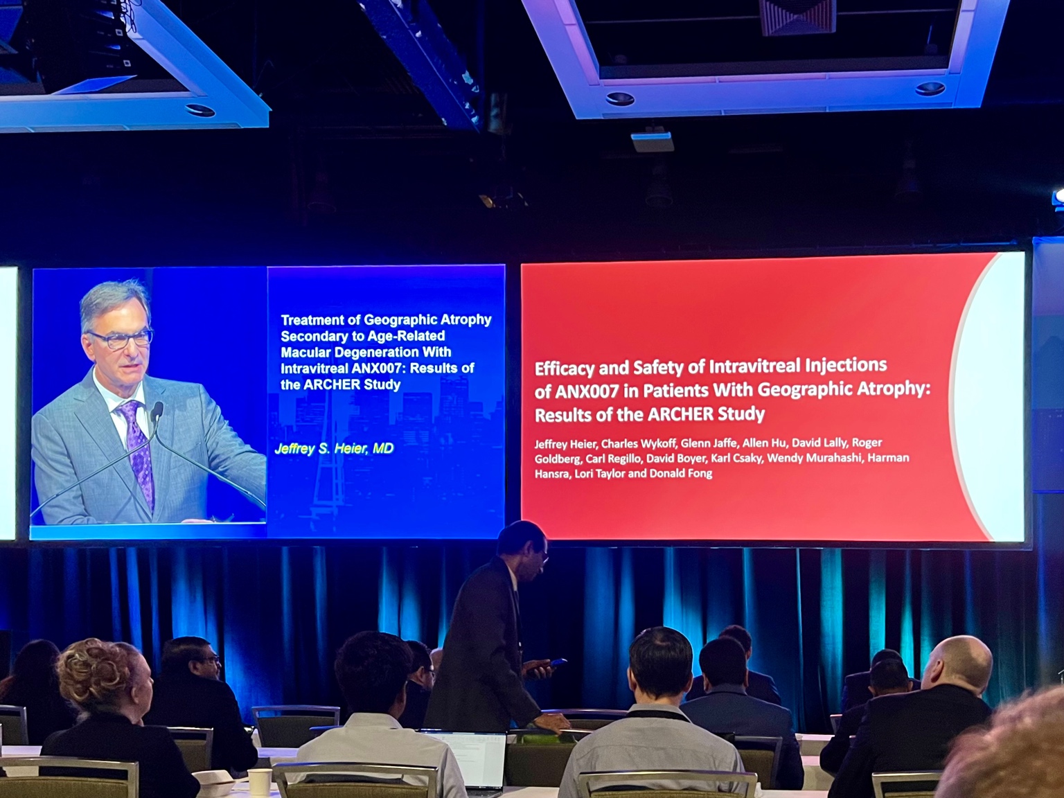 A group of people sitting at a table in front of a screen Description automatically generated