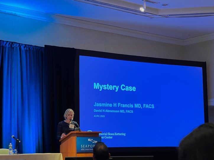 A person standing at a podium in front of a large screen Description automatically generated with medium confidence