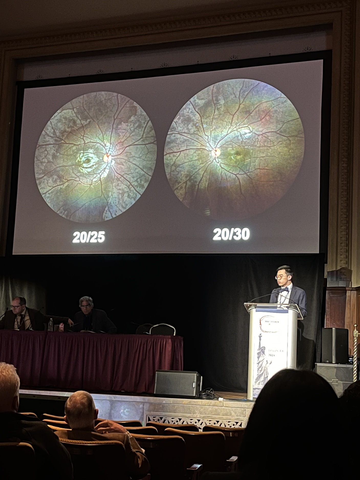 A person standing at a podium with a large screen Description automatically generated