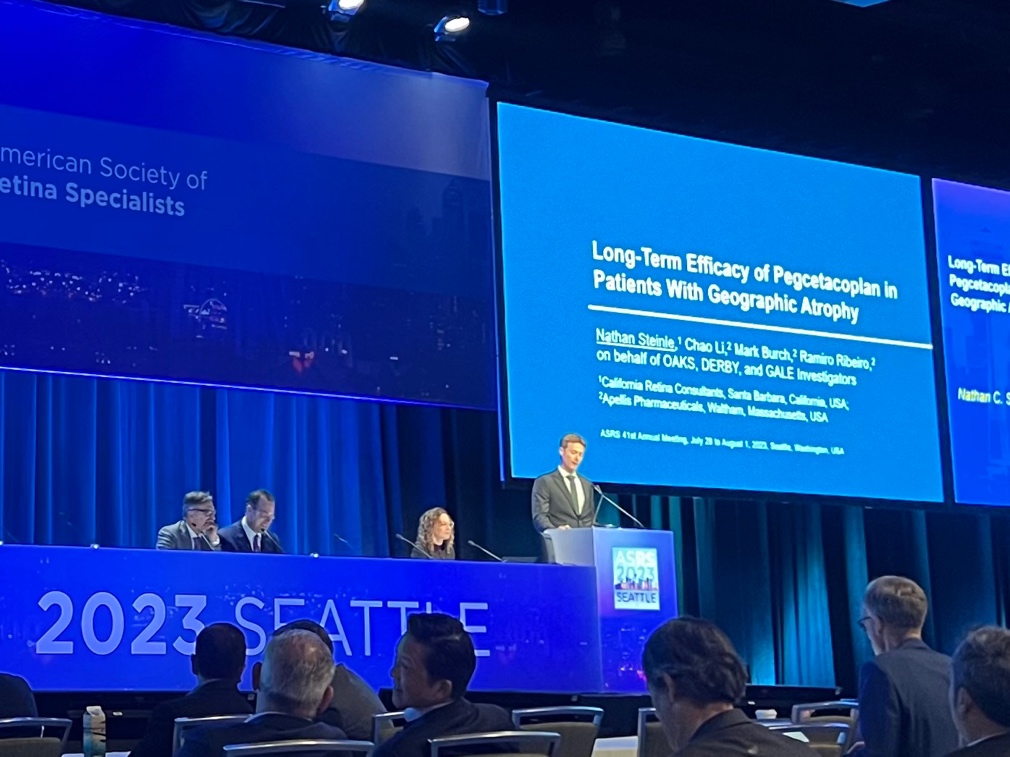 A person standing at a podium with a large screen behind him  Description automatically generated